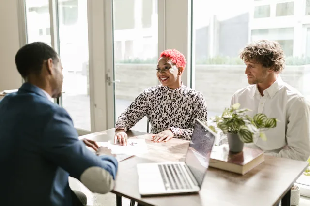 Three professionals meeting in a sunny office discussing finance with smiles. Credit unions: which services to weigh for your business
